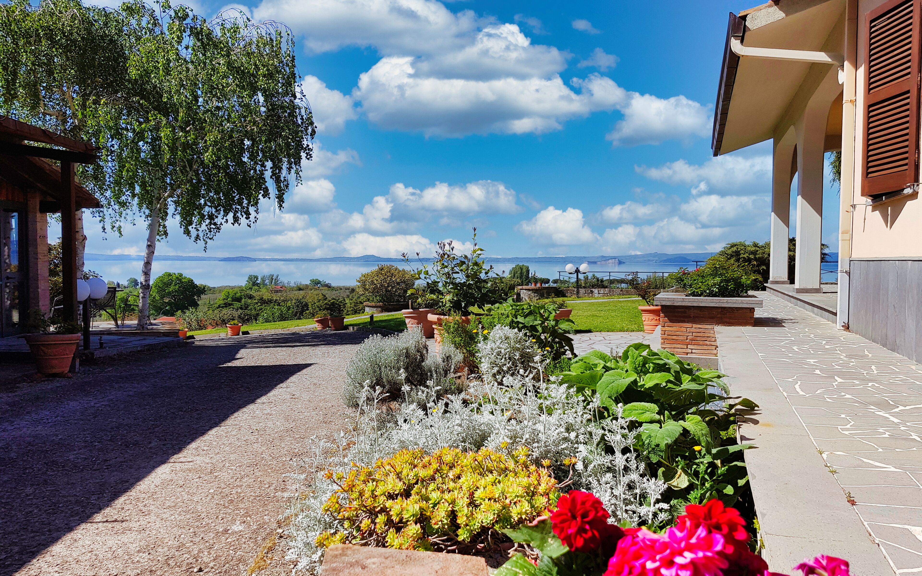 A garden with potted plants and flowers, a pathway, and a view of the sea.