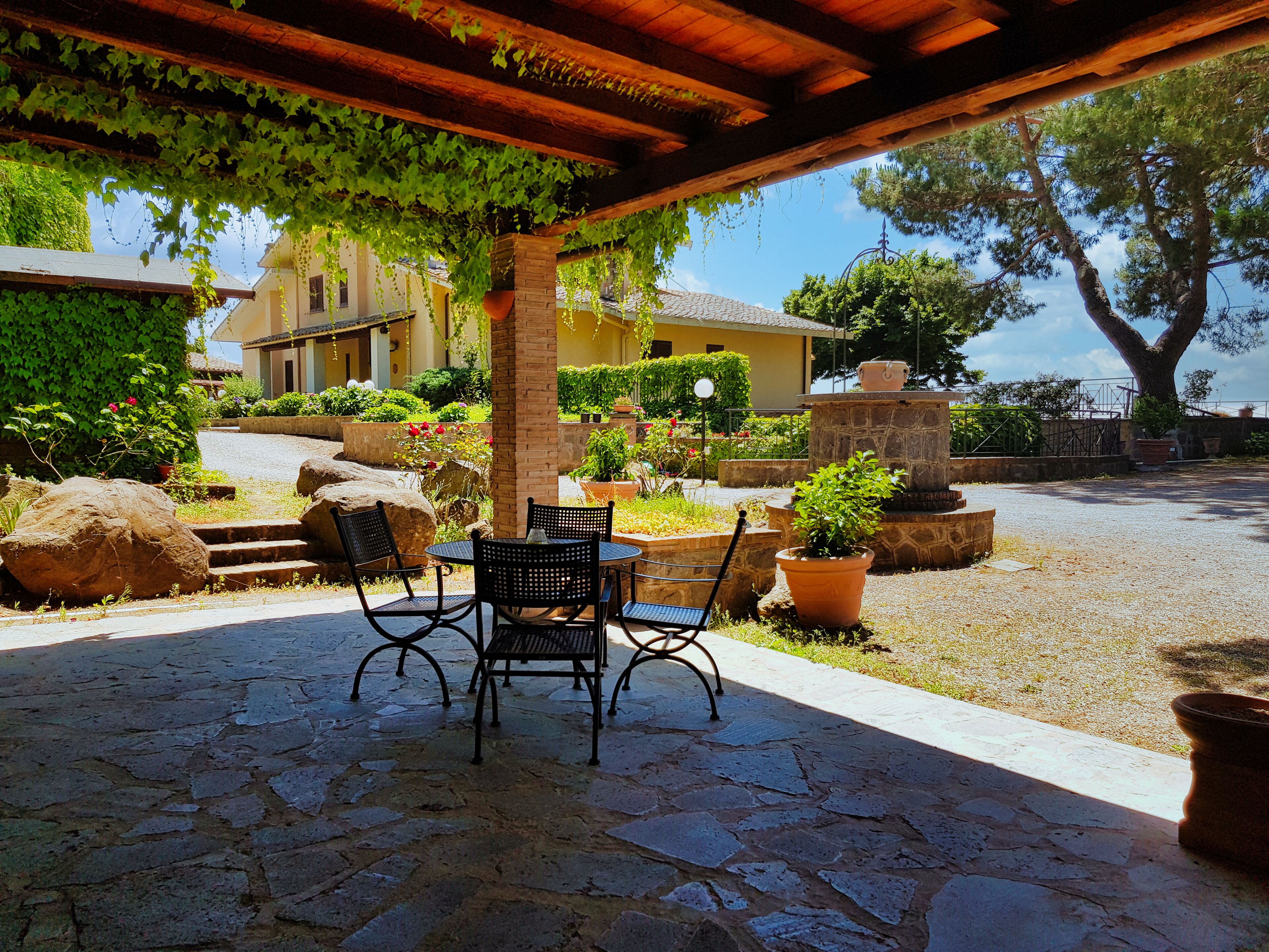 A covered patio with stone flooring, two chairs, and potted plants.