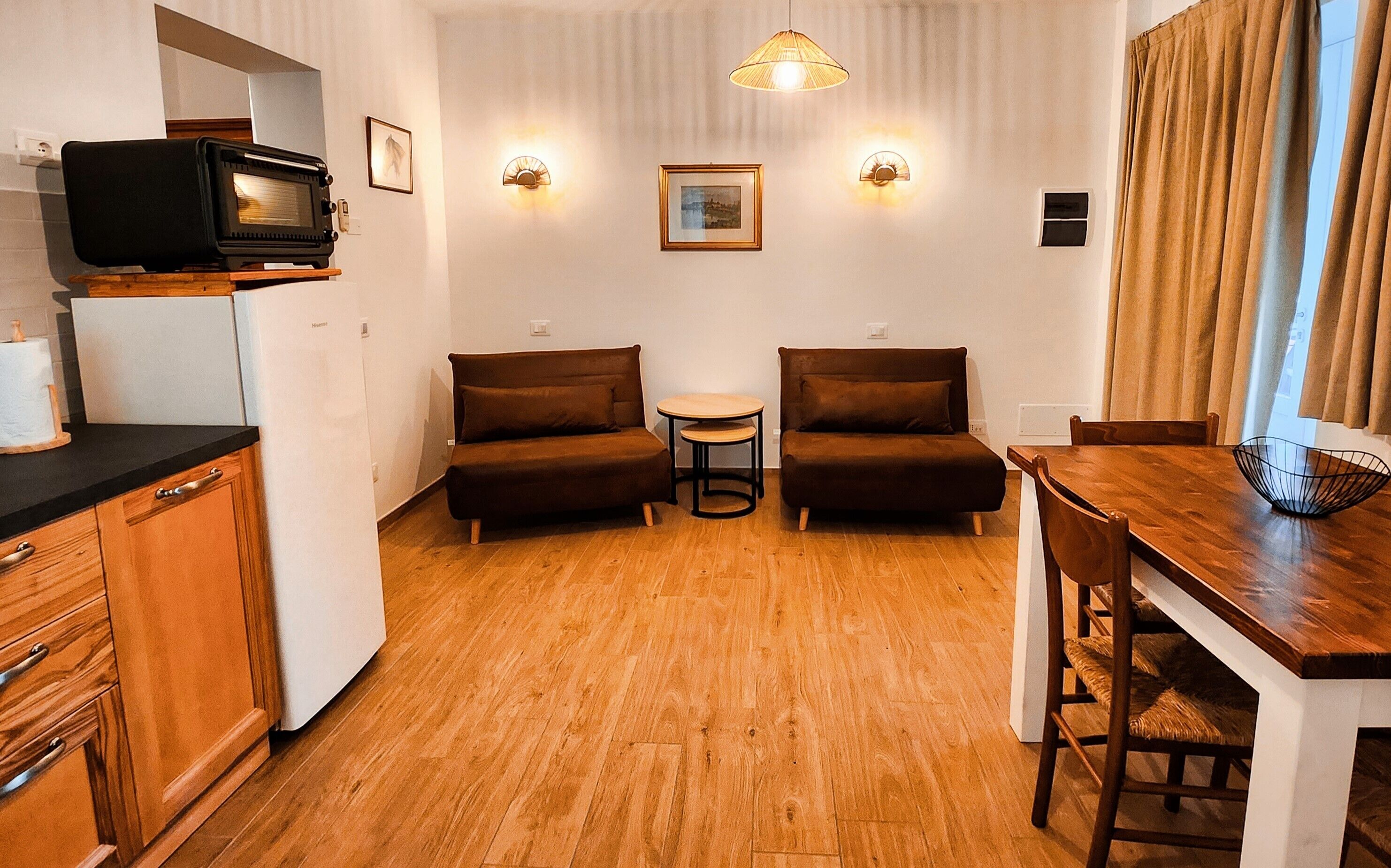 A compact living space with a kitchenette, two sofas, a small round table, and a wooden dining table.