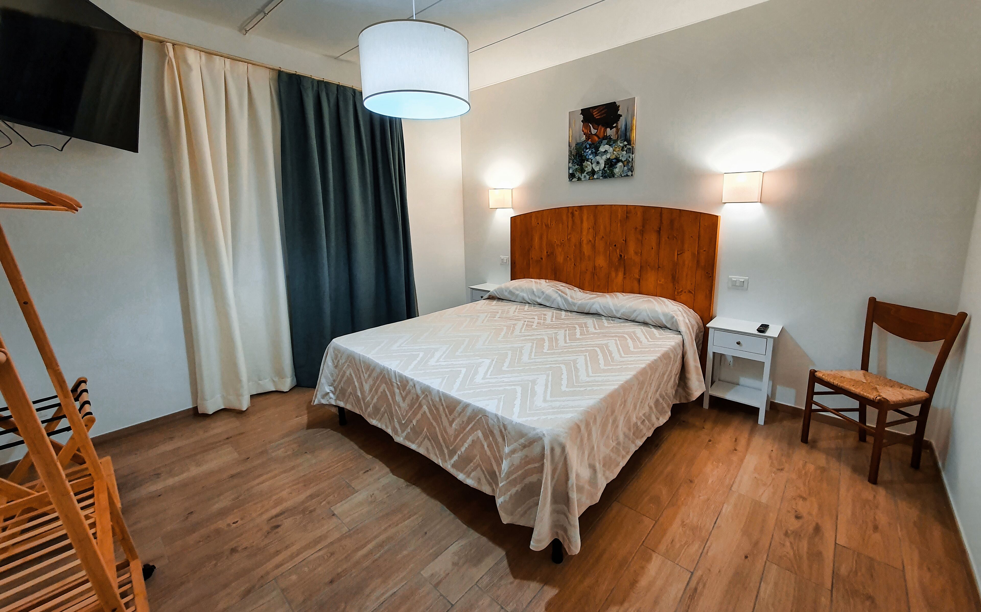 Ein ordentlich eingerichtetes Schlafzimmer mit einem hölzernen Bett, einem Nachttisch, einem Sessel und einem Gemälde an der Wand.