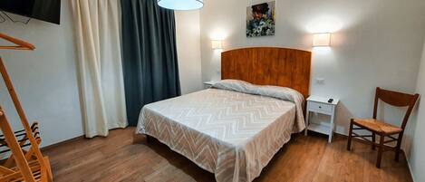 Ein ordentlich eingerichtetes Schlafzimmer mit einem hölzernen Bett, einem Nachttisch, einem Sessel und einem Gemälde an der Wand.