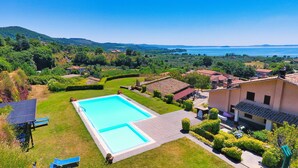 A swimming pool surrounded by a well-maintained lawn, with a view of a lake and hills in the background. - Le vigne (Bolsena)
