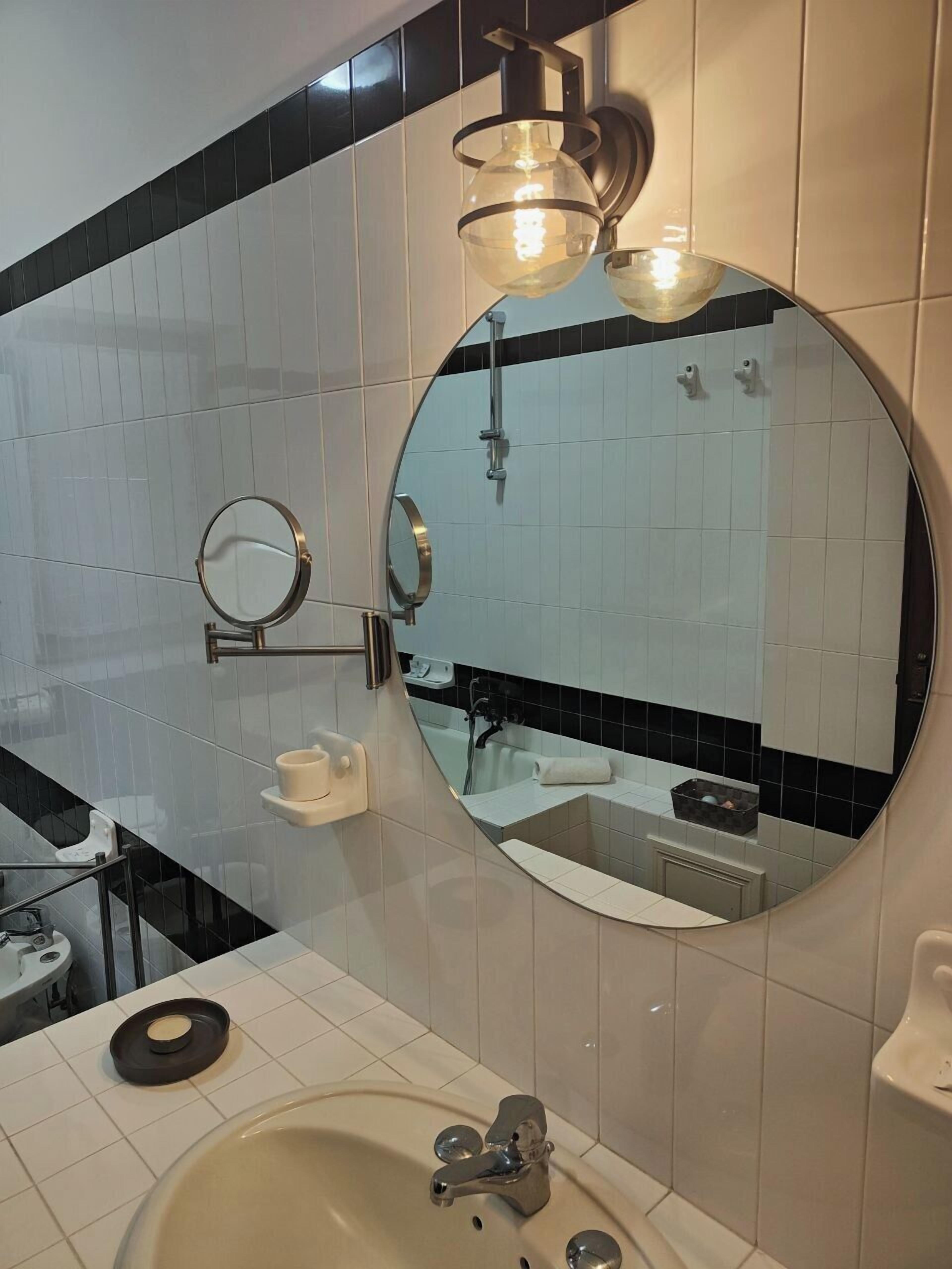A bathroom with a round mirror, a sink, and a shower.