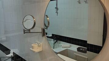 A bathroom with a round mirror, a sink, and a shower.
