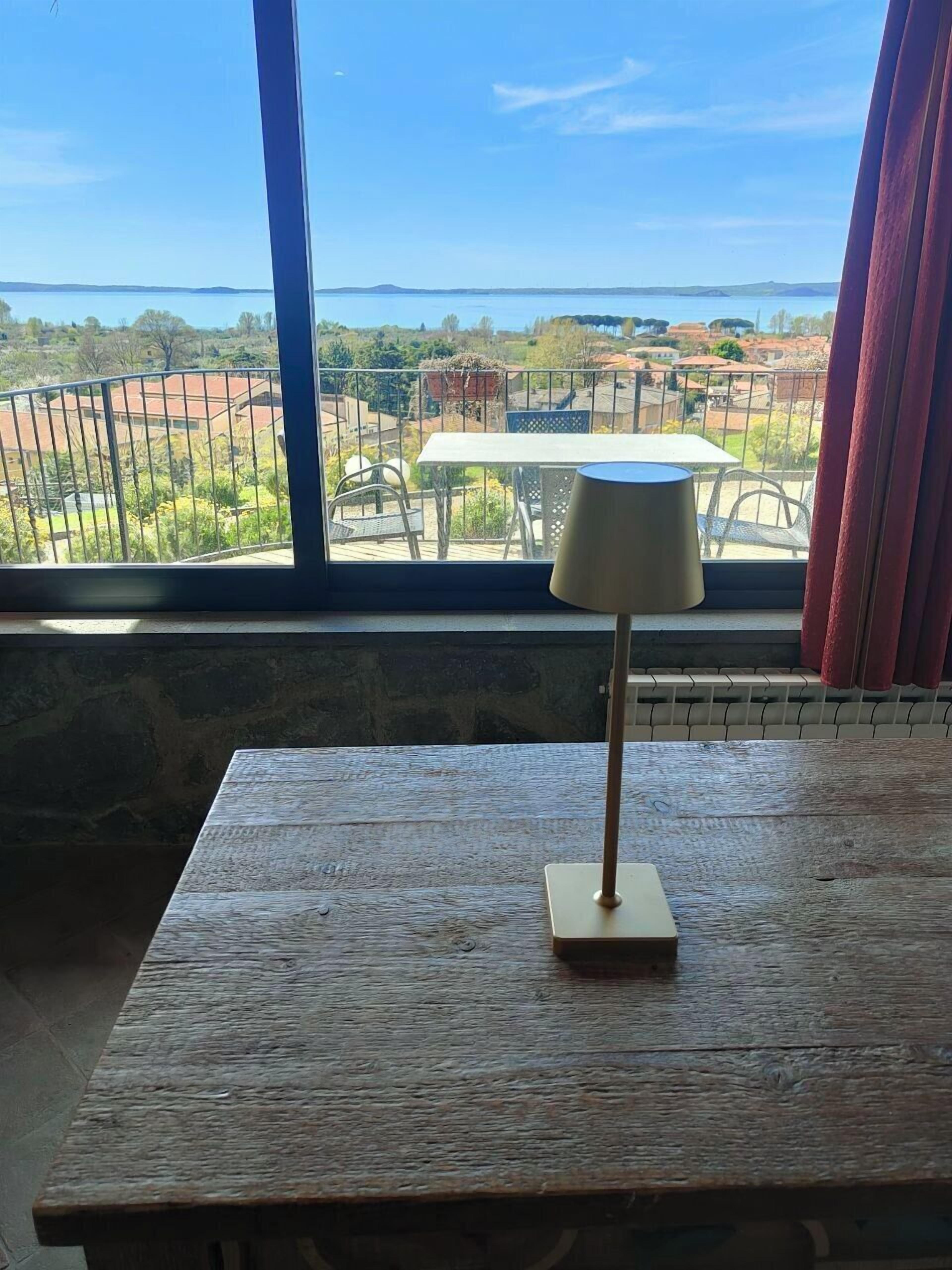 Ein Holztisch mit einer Lampe in einem Raum mit einem großen Fenster, das auf einen Garten und eine ferne Hügellandschaft blickt.