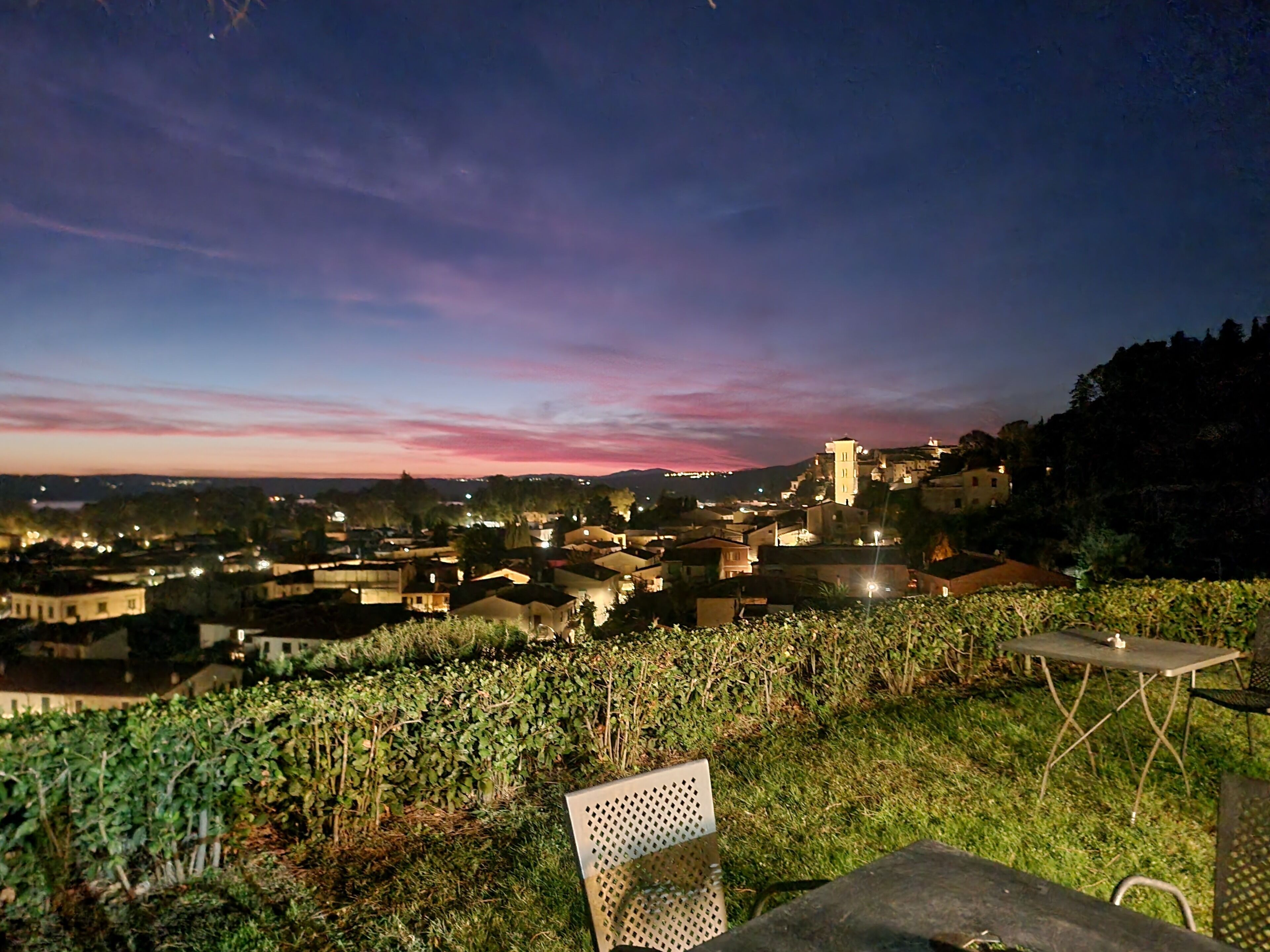 Viñedo con una mesa y una silla, con vistas a un pueblo con edificios históricos y una iglesia en la colina.