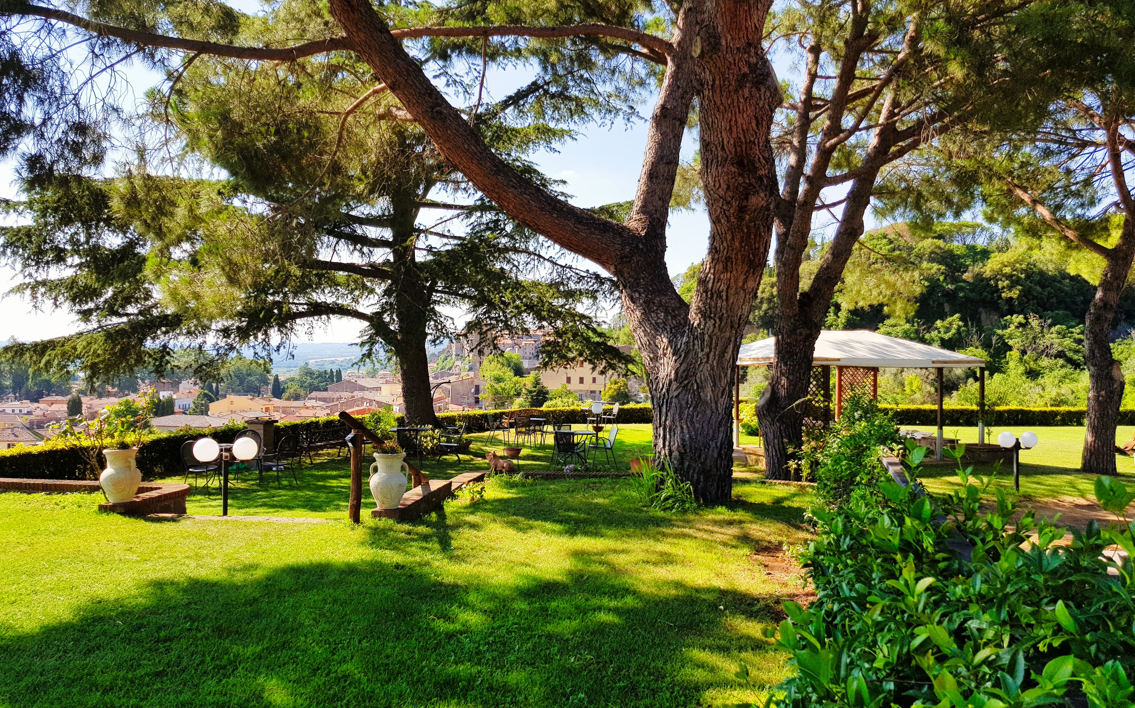 A lush garden with a gazebo, seating areas, and a view of a distant town.