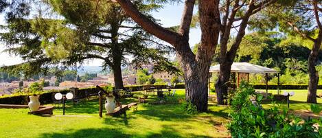 A lush garden with a gazebo, seating areas, and a view of a distant town.