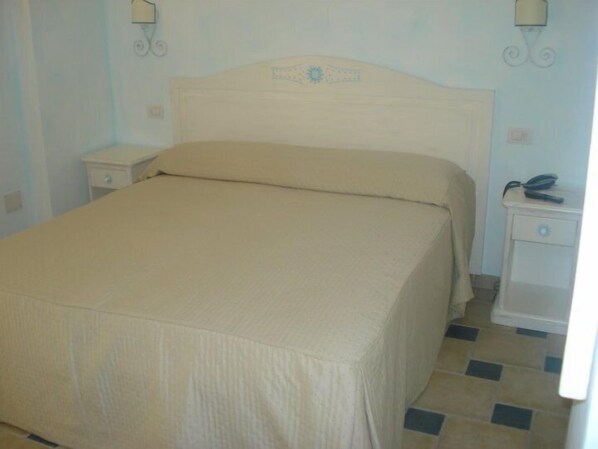 Un dormitorio con cama, mesitas de noche y una lámpara fijada a la pared.