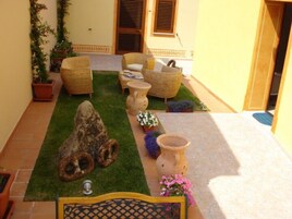 Un pequeño espacio al aire libre con mobiliario de mimbre, una escultura de piedra y plantas en macetas.