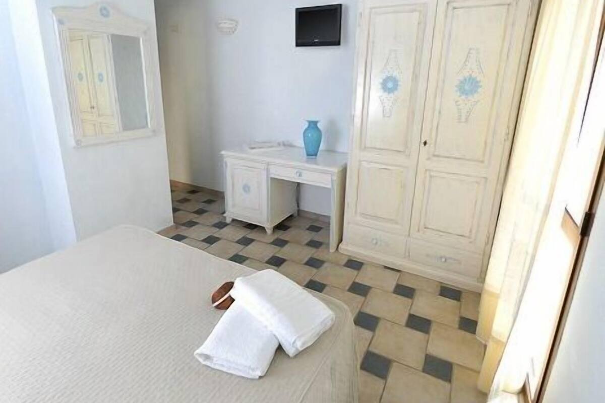 A bedroom with a bed, a desk, a wardrobe, and a television on the wall.