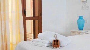 A hotel room with a bed, a wooden door, a blue vase, and a small table with a lamp. - Hotel Patti (Golfo Aranci)