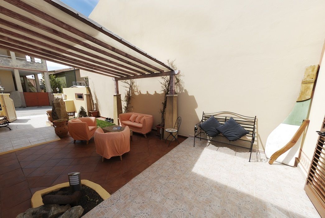 Un'area patio esterna con una zona salotto coperta, un piccolo tavolo e un braciere.