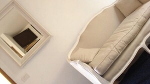 A room with a white sofa, a small white cabinet with a flat-screen TV, and a blue blanket on the floor. - Hotel Patti (Golfo Aranci)