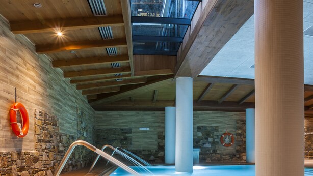 Piscina interior con techo de madera y paredes de piedra, con un flotador y una vista despejada del cielo a través del techo.