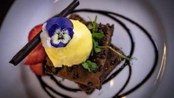 A dessert with chocolate cake, a scoop of ice cream, a flower, and a chocolate drizzle on a plate.