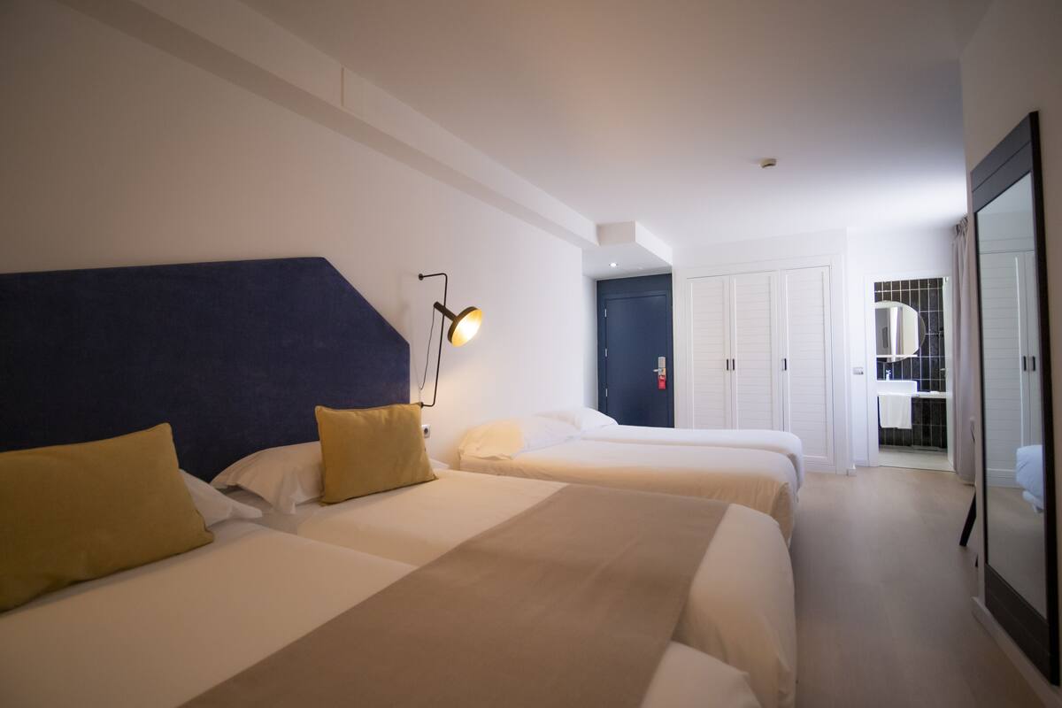 A hotel room with two beds, a dark blue headboard, a bedside lamp, and a view of the bathroom.