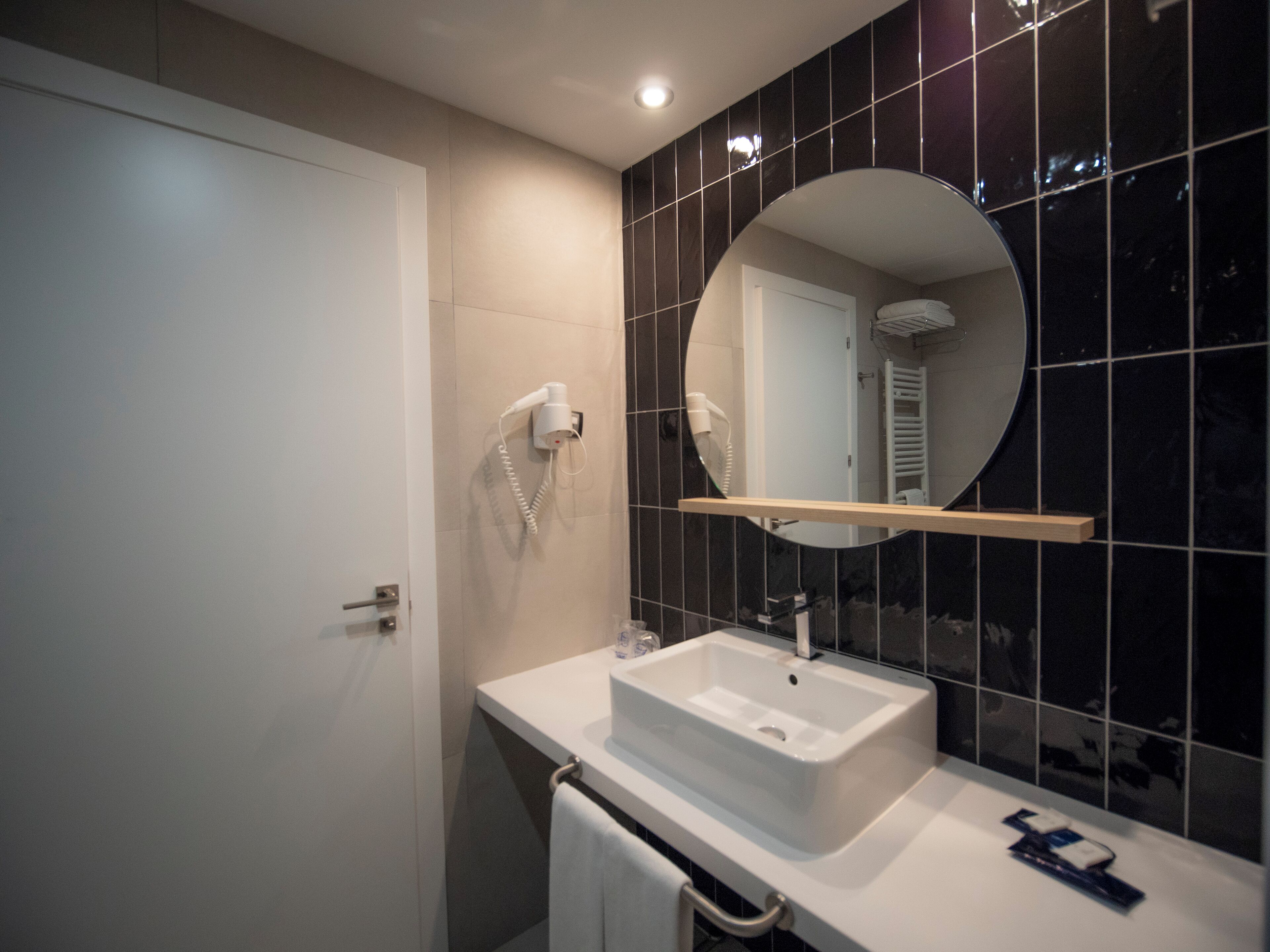A modern bathroom with a white sink, a mirror, and a hairdryer mounted on the wall.