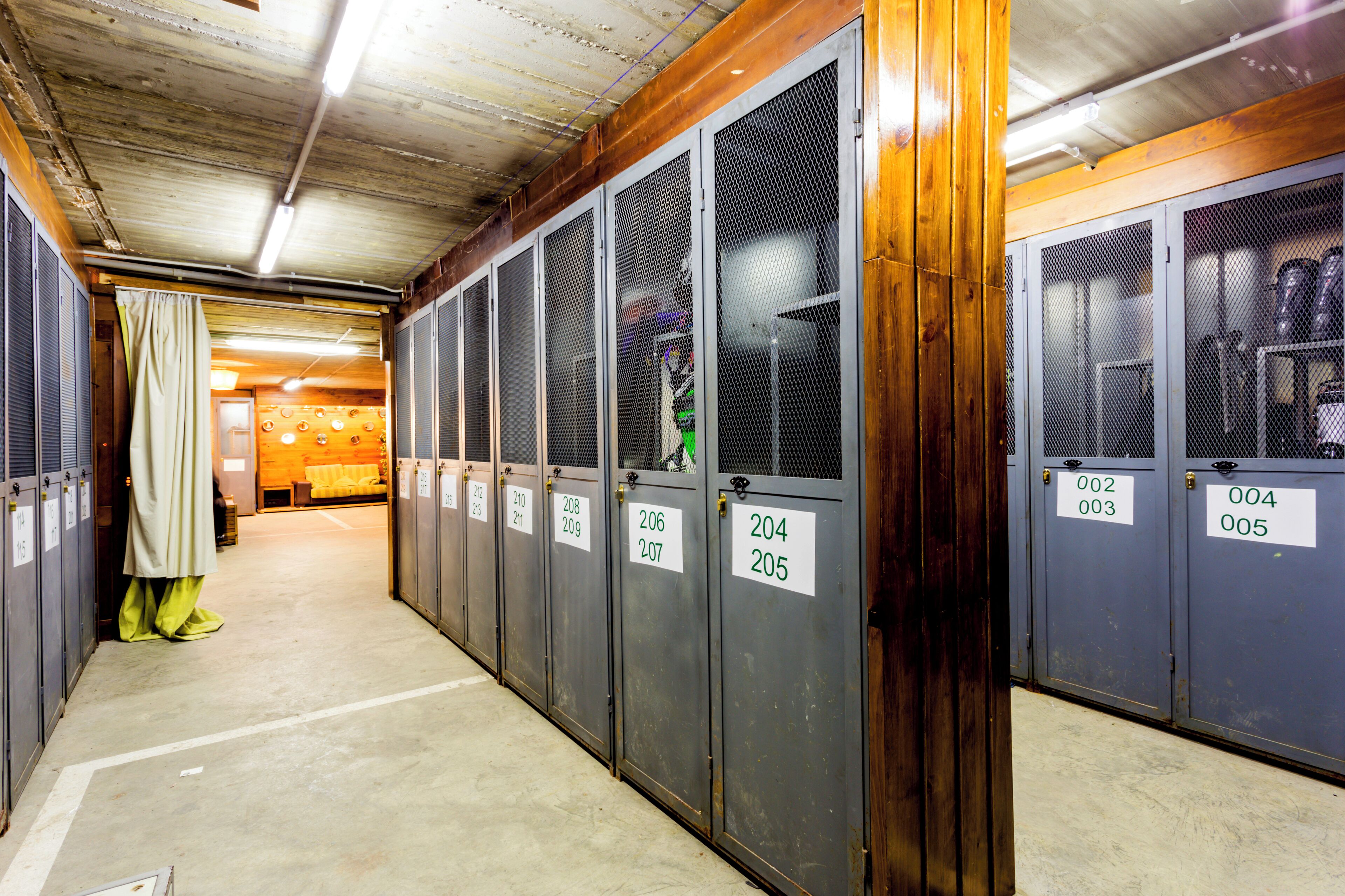 A row of metal lockers with numbered tags, a concrete floor, and a wooden ceiling.