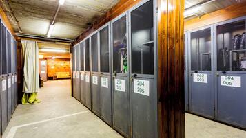A row of metal lockers with numbered tags, a concrete floor, and a wooden ceiling.