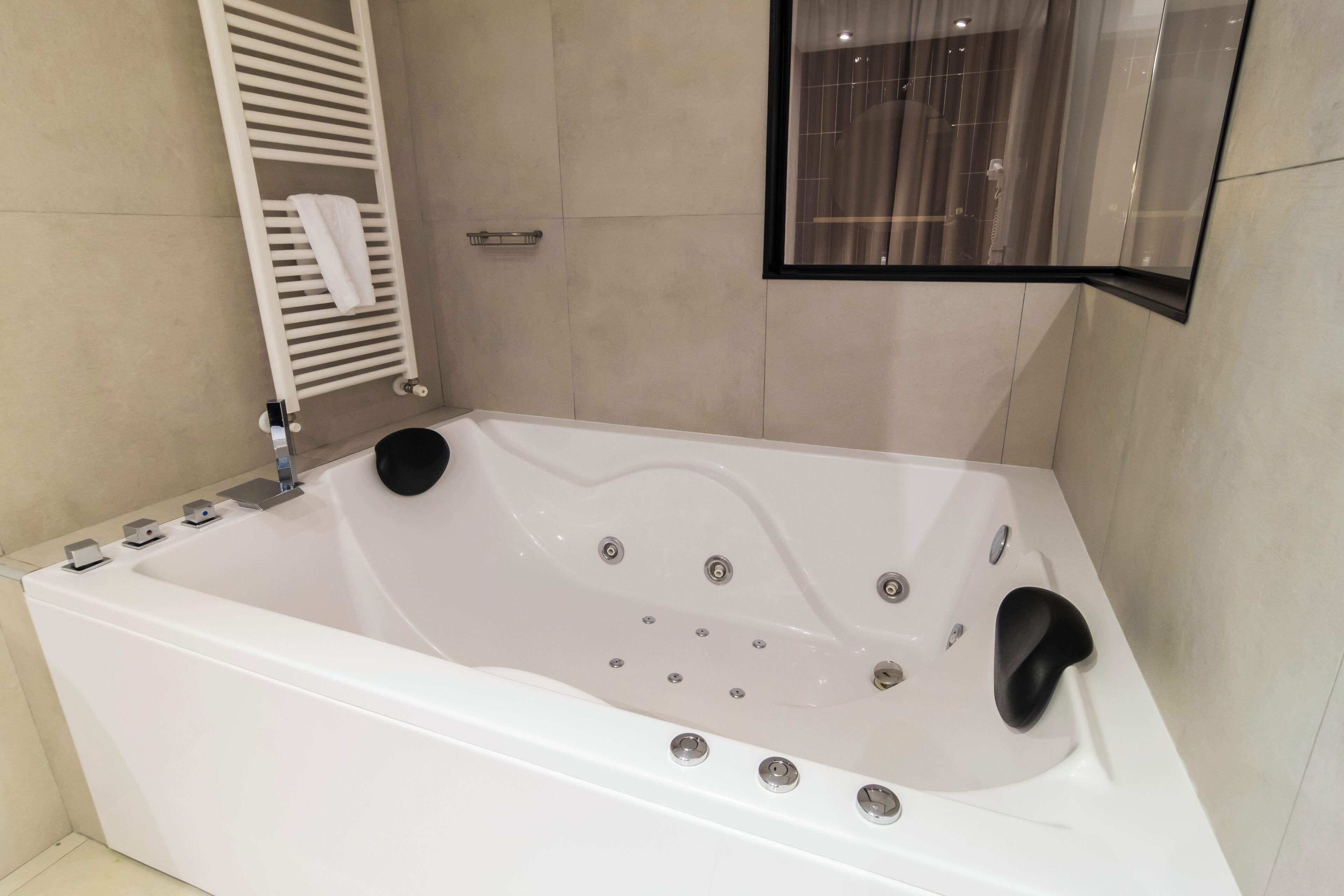 Un baño moderno con una bañera blanca, un perchero para toallas y un ventanal con cortinas.