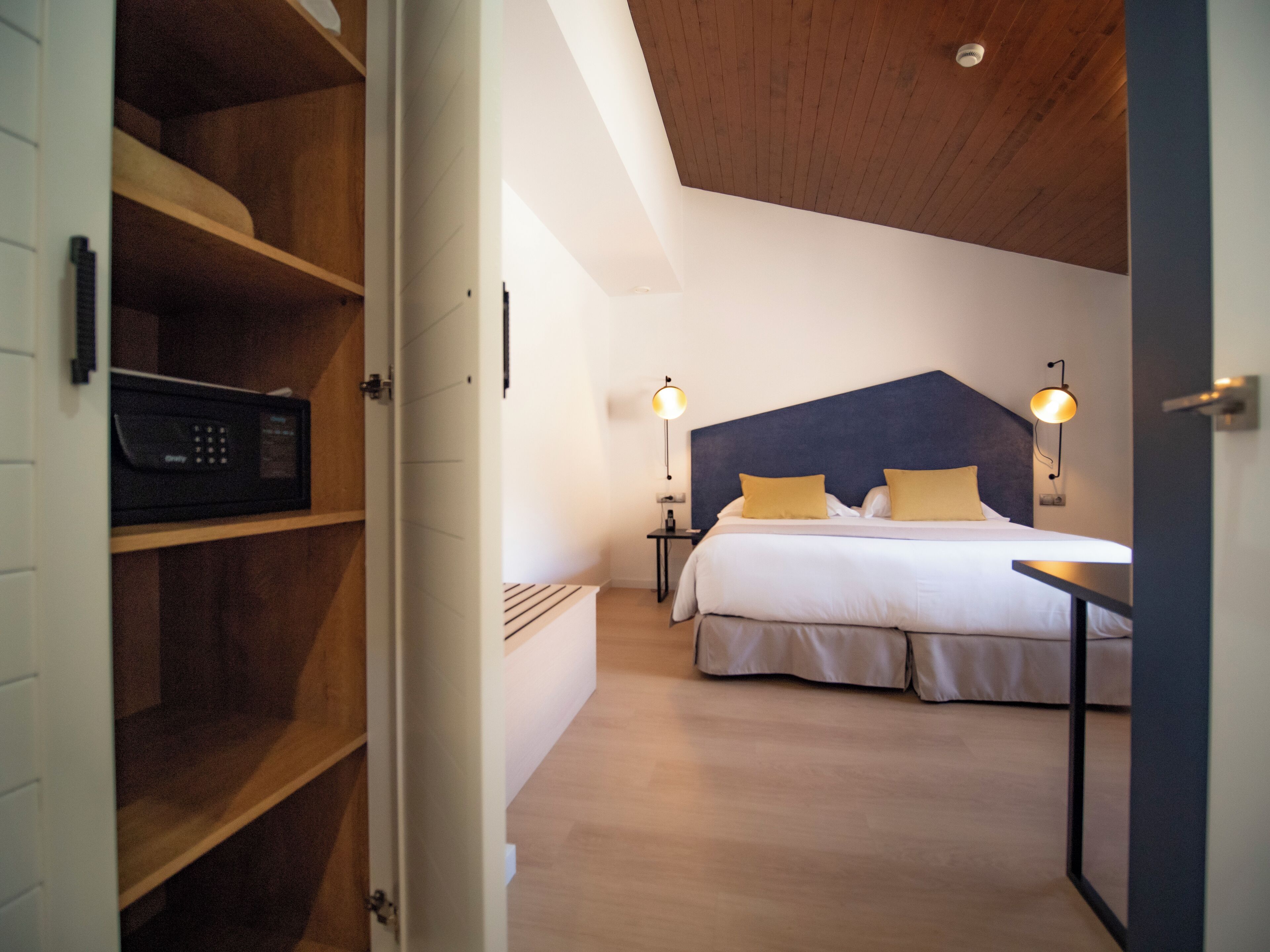A bedroom with a bed, bedside lamps, a wooden shelf with a microwave, and a ceiling light.