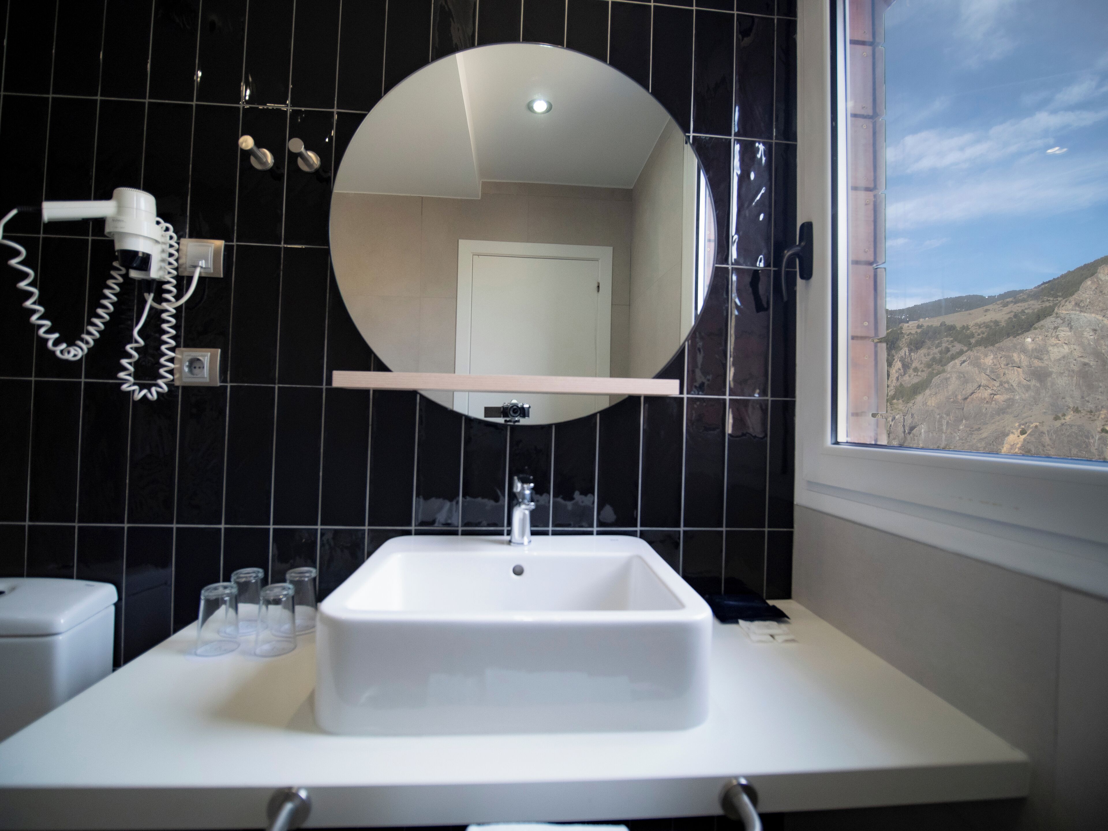 A bathroom with a white sink, a round mirror, and a hairdryer on the wall.