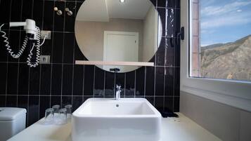 A bathroom with a white sink, a round mirror, and a hairdryer on the wall.