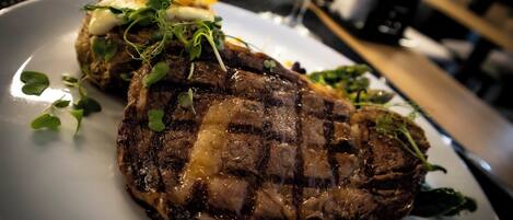 Um bife com exterior carbonizado, acompanhado de vegetais e batatas assadas.