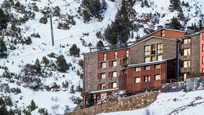 Un hotel moderno con fachada de piedra, varias ventanas y un telesilla al fondo.