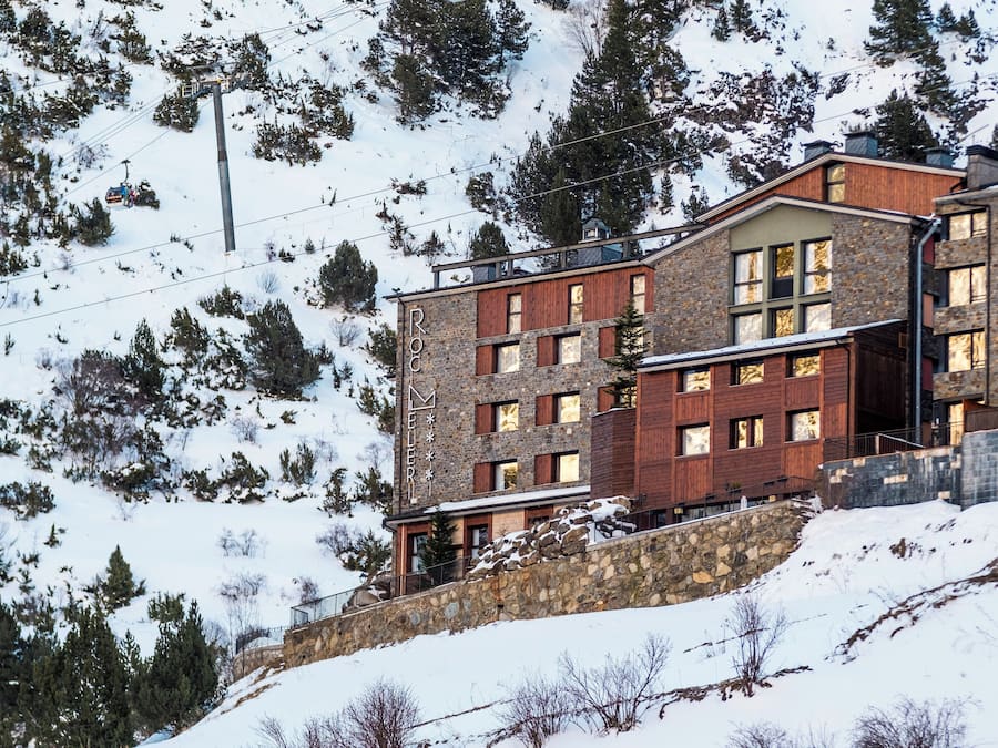 A modern hotel with a stone facade, multiple windows, and a ski lift in the background.