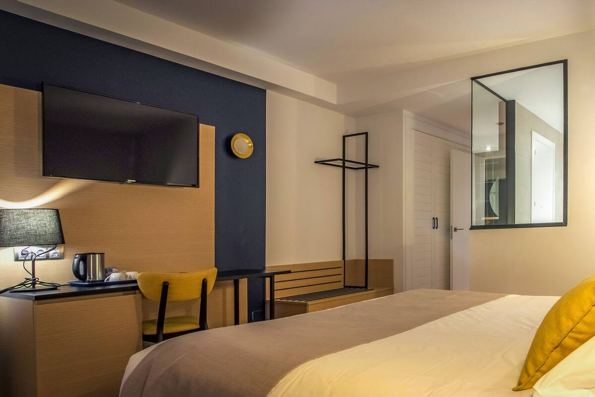 A hotel room with a bed, a desk with a lamp, a chair, a TV, and a mirror.