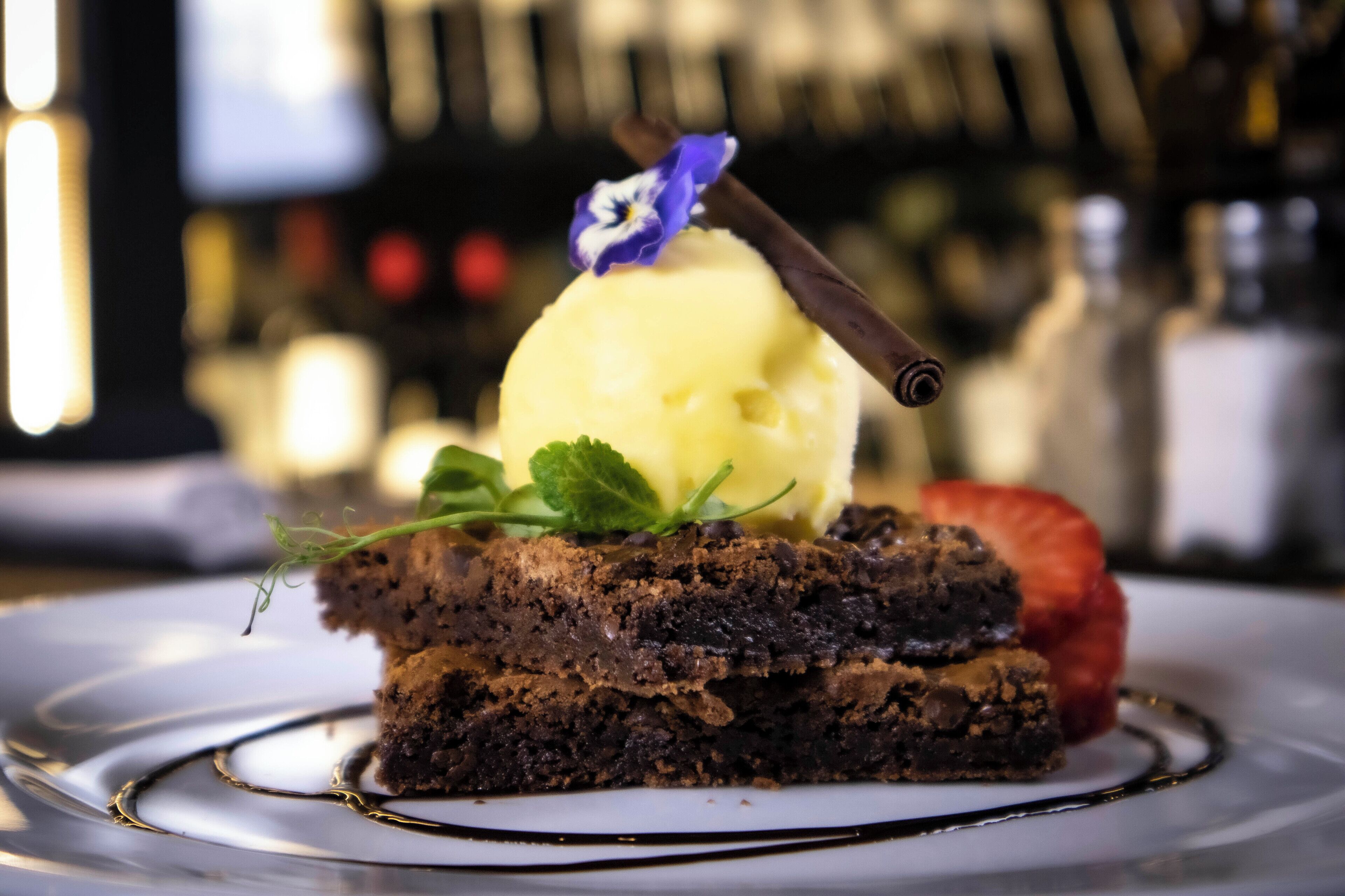 Un postre con pastel de chocolate, una bola de helado de vainilla, un palito de chocolate, una fresa y una hoja de menta en un plato.