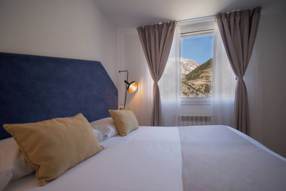 A neatly made bed with two pillows, a bedside lamp, and a window with curtains.