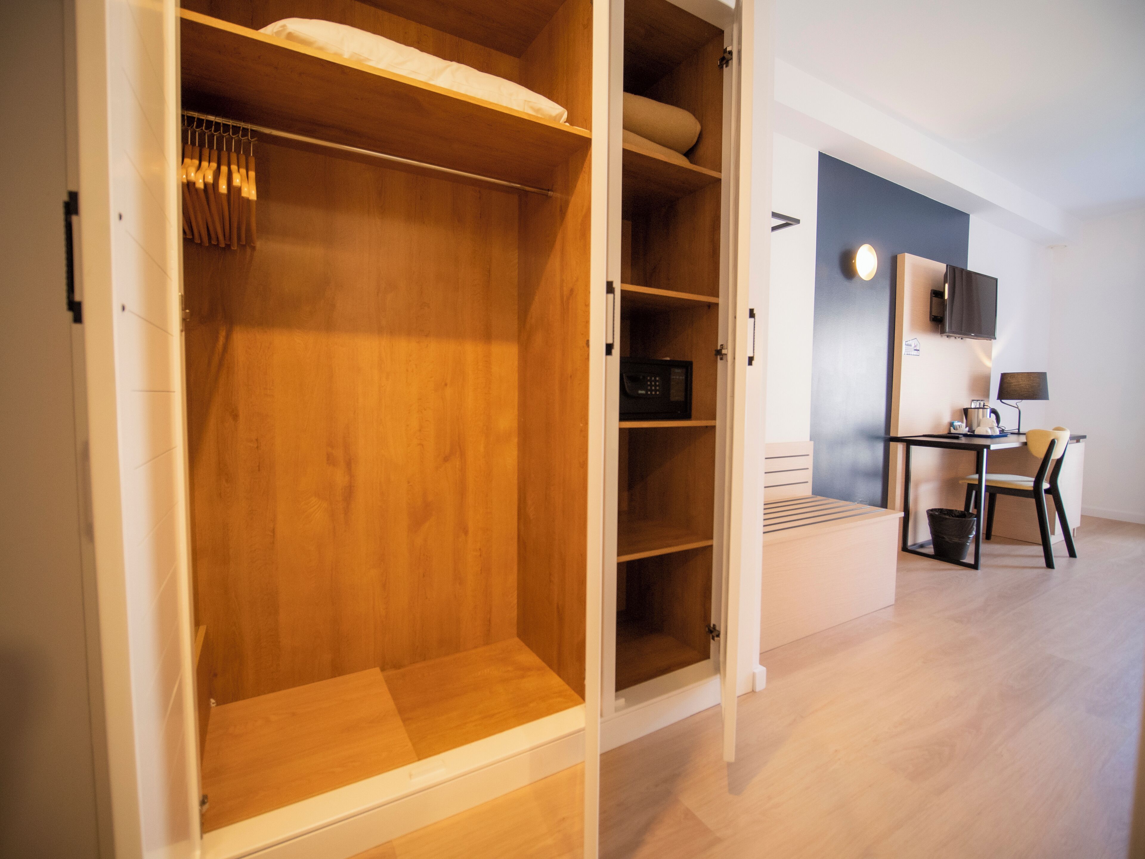 A walk-in closet with wooden shelves and hanging space, a desk with a chair, and a small trash bin.