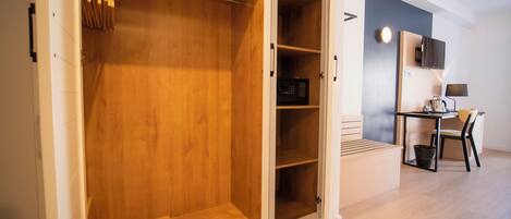 A walk-in closet with wooden shelves and hanging space, a desk with a chair, and a small trash bin.