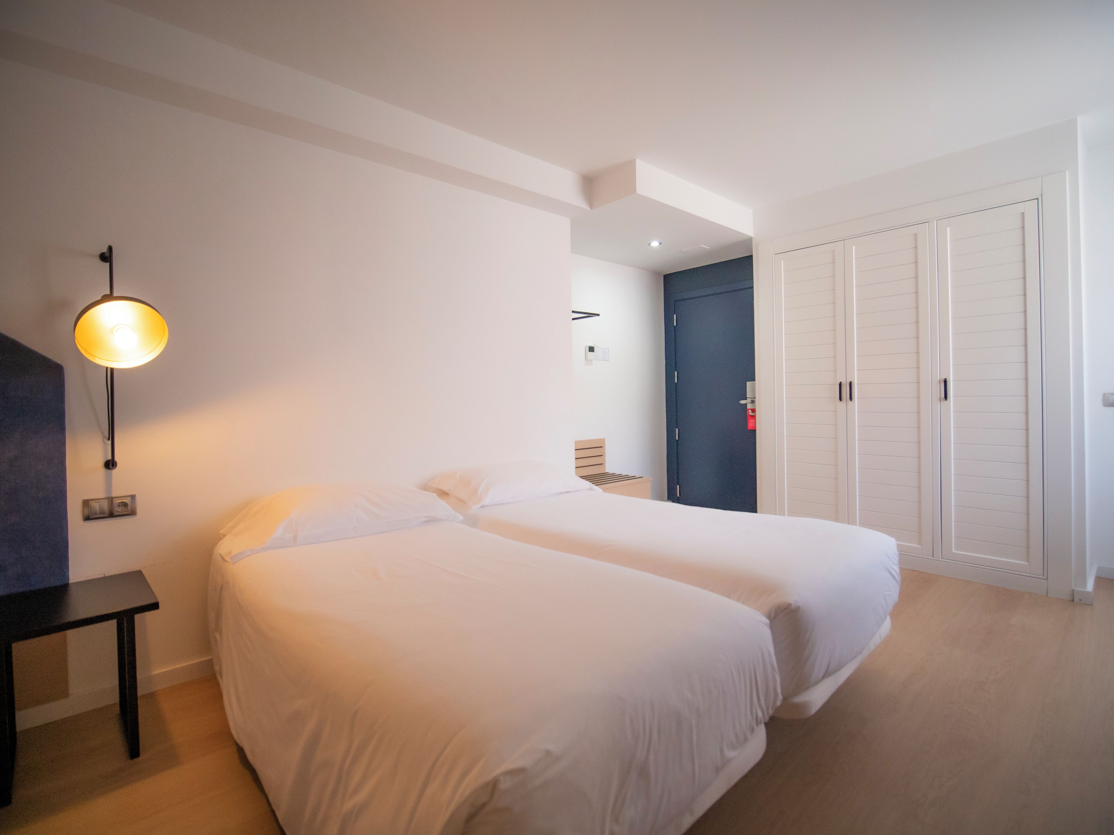 Ein Hotelzimmer mit zwei Betten, einem Schreibtisch, einer Lampe und einem Kleiderschrank.