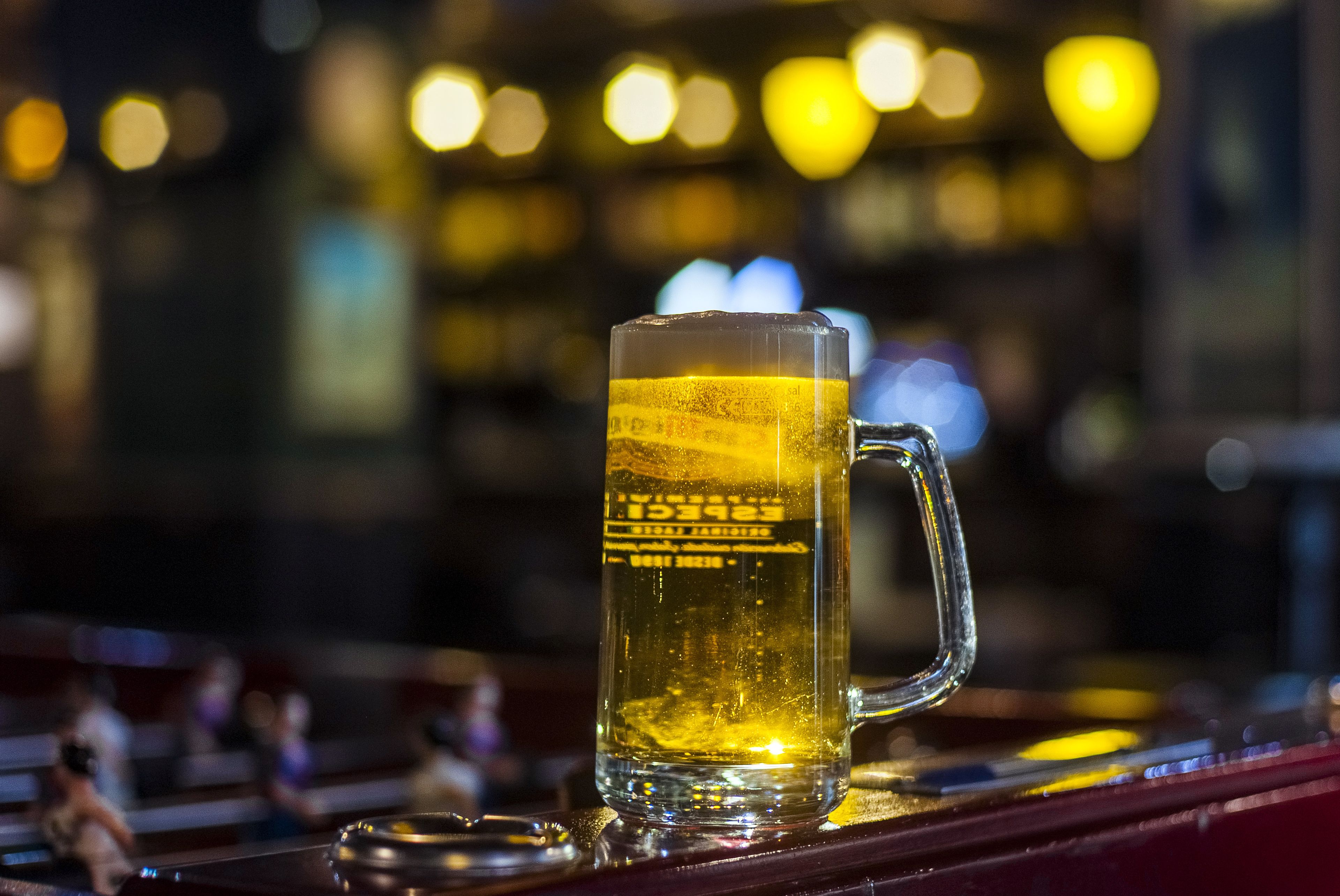 A clear glass mug with a label, placed on a bar counter with a blurred background of lights.