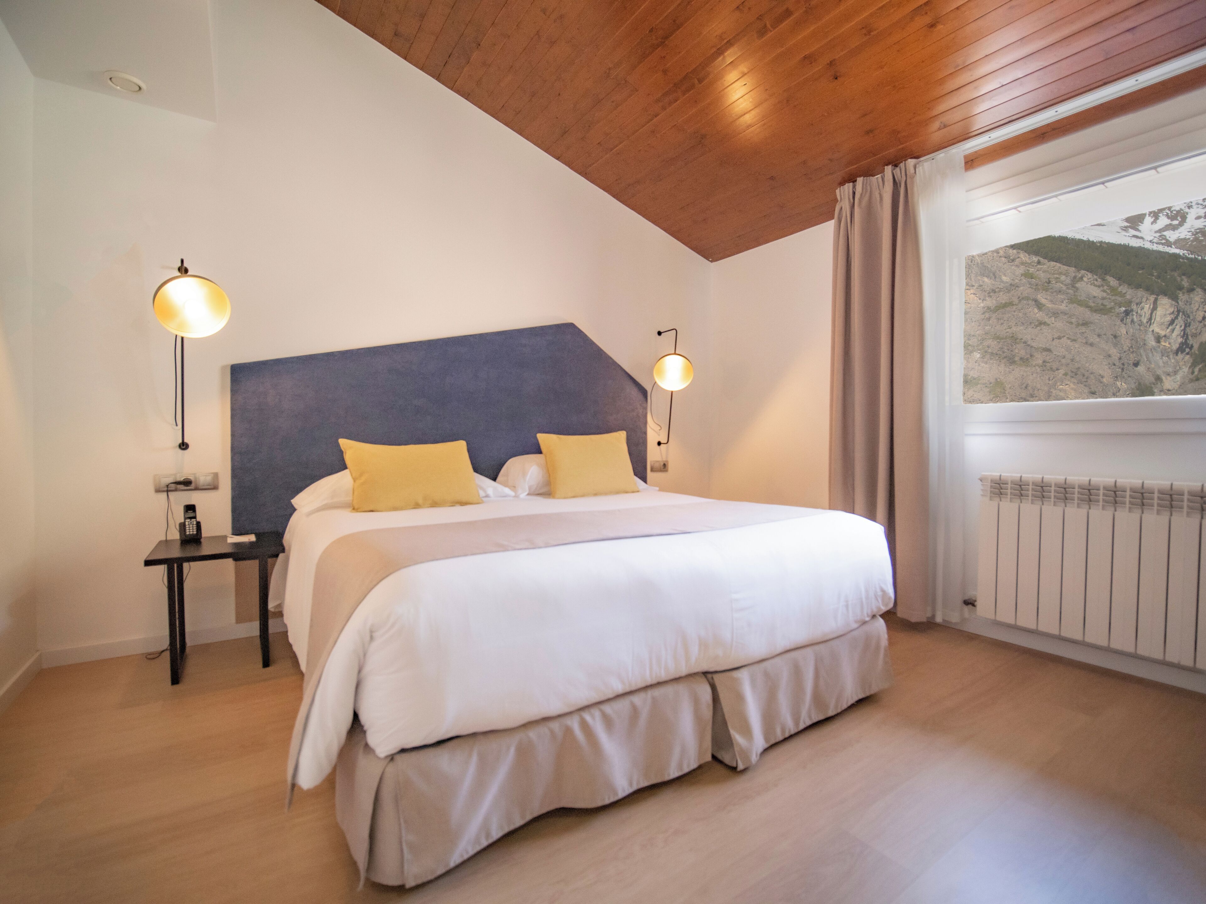 A bedroom with a bed, bedside tables, and a window with a view of a mountain.