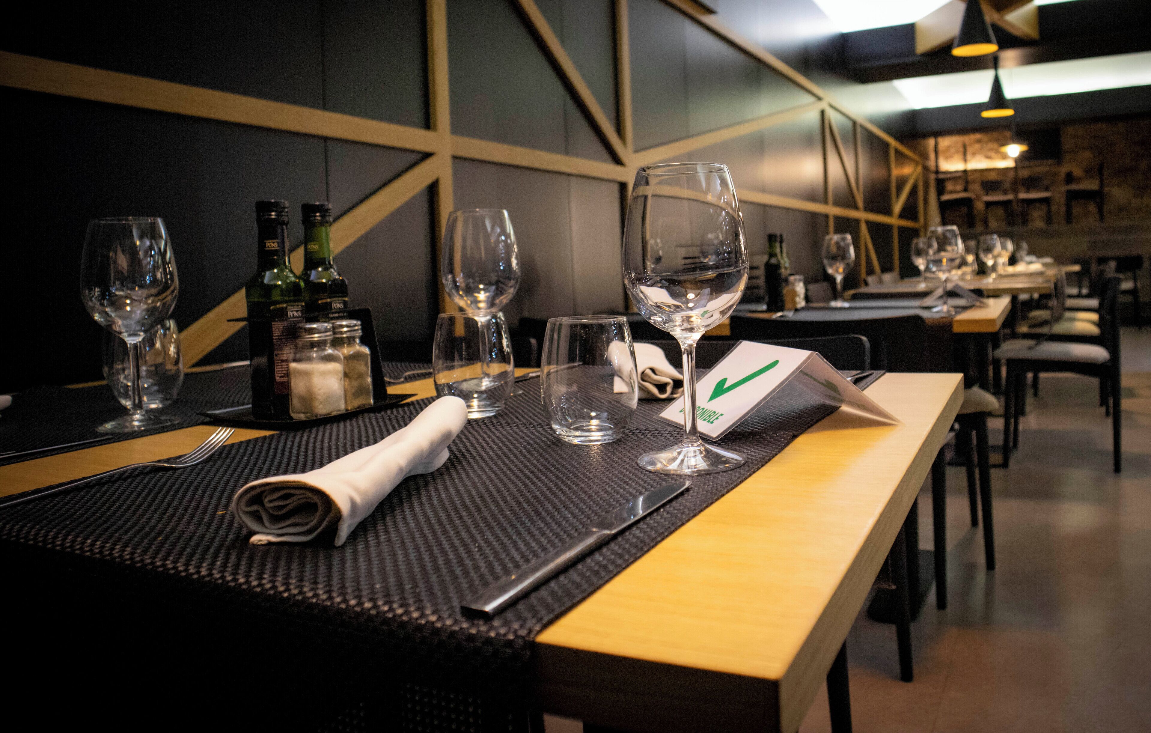 Een restaurantscène met gedekte tafels, inclusief wijnkaraffen, flessen en bestek.