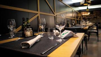 A restaurant setting with tables set for dining, including wine glasses, bottles, and cutlery.