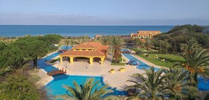 Um resort com uma piscina grande, área coberta e vista para o mar.