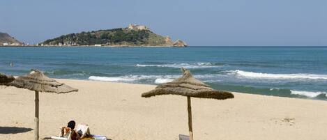 Une plage avec deux parasols en chaume et des chaises longues.