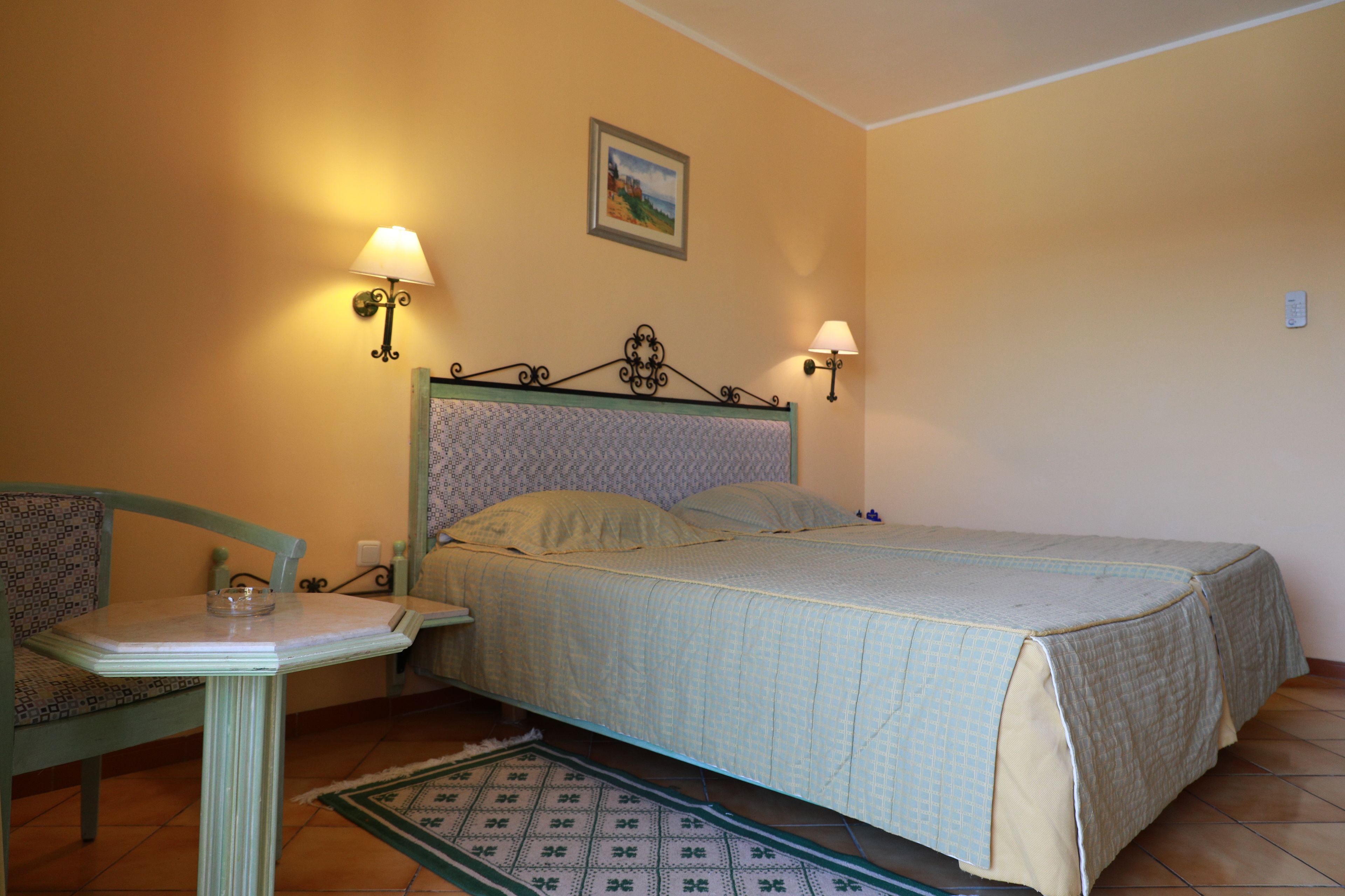 Une chambre à coucher avec un lit, des lampes de chevet, une chaise, une table et un tableau au mur.