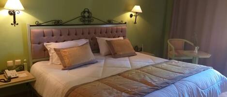 Een hotelkamer met een groot bed, twee bedlampen, een stoel en een lijst aan de muur.