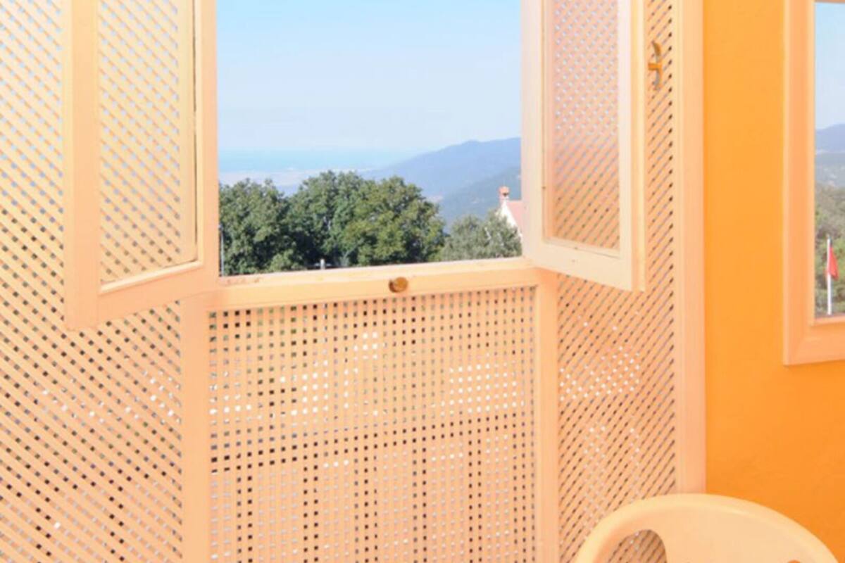 A small balcony with white chairs and a table, a view of greenery and mountains, and a yellow wall.