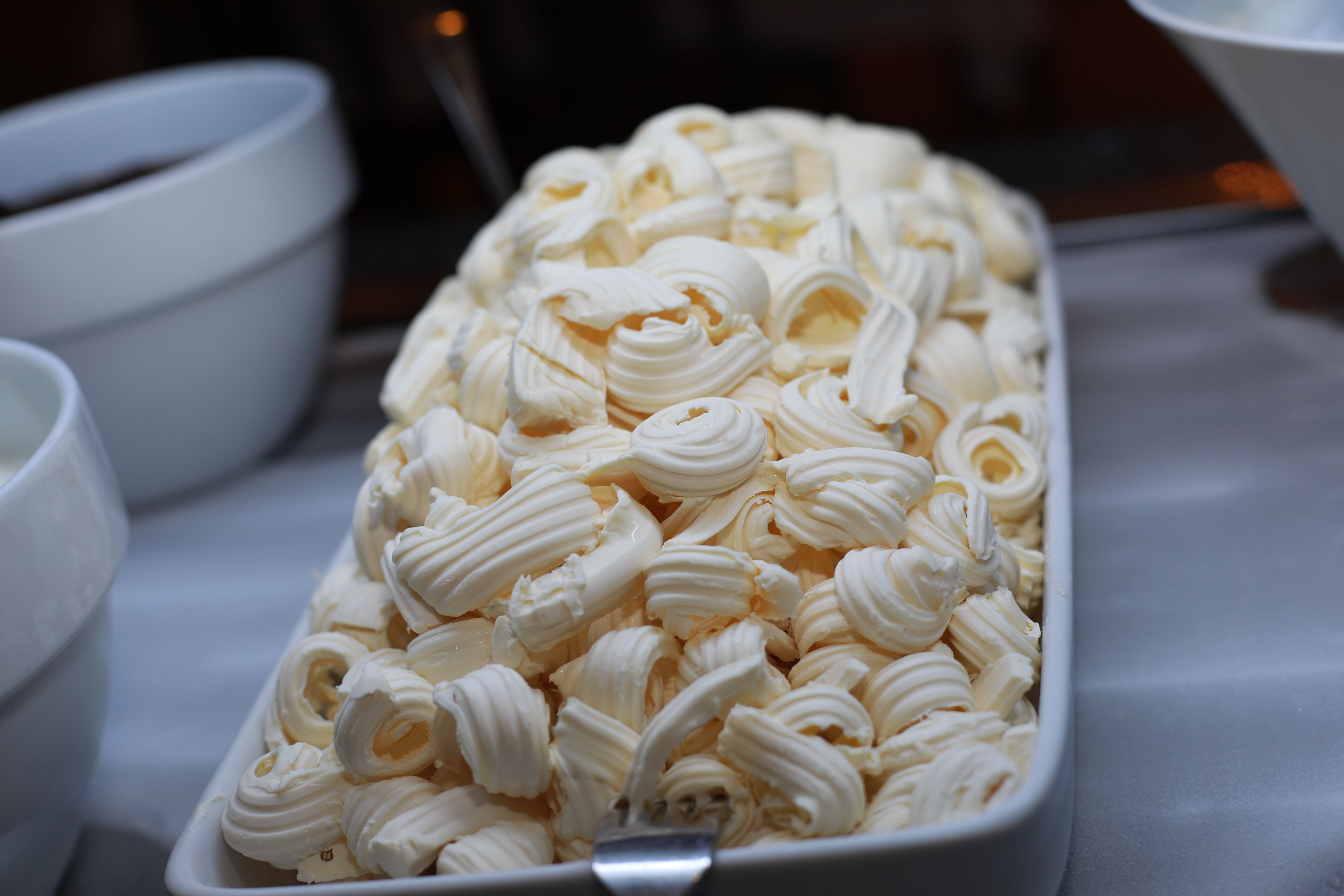 Eine weiße, rechteckige Servierschale gefüllt mit weißem, spiralförmigem Inhalt, vermutlich ein Dessert, auf einem Tisch mit weißer Tischdecke.