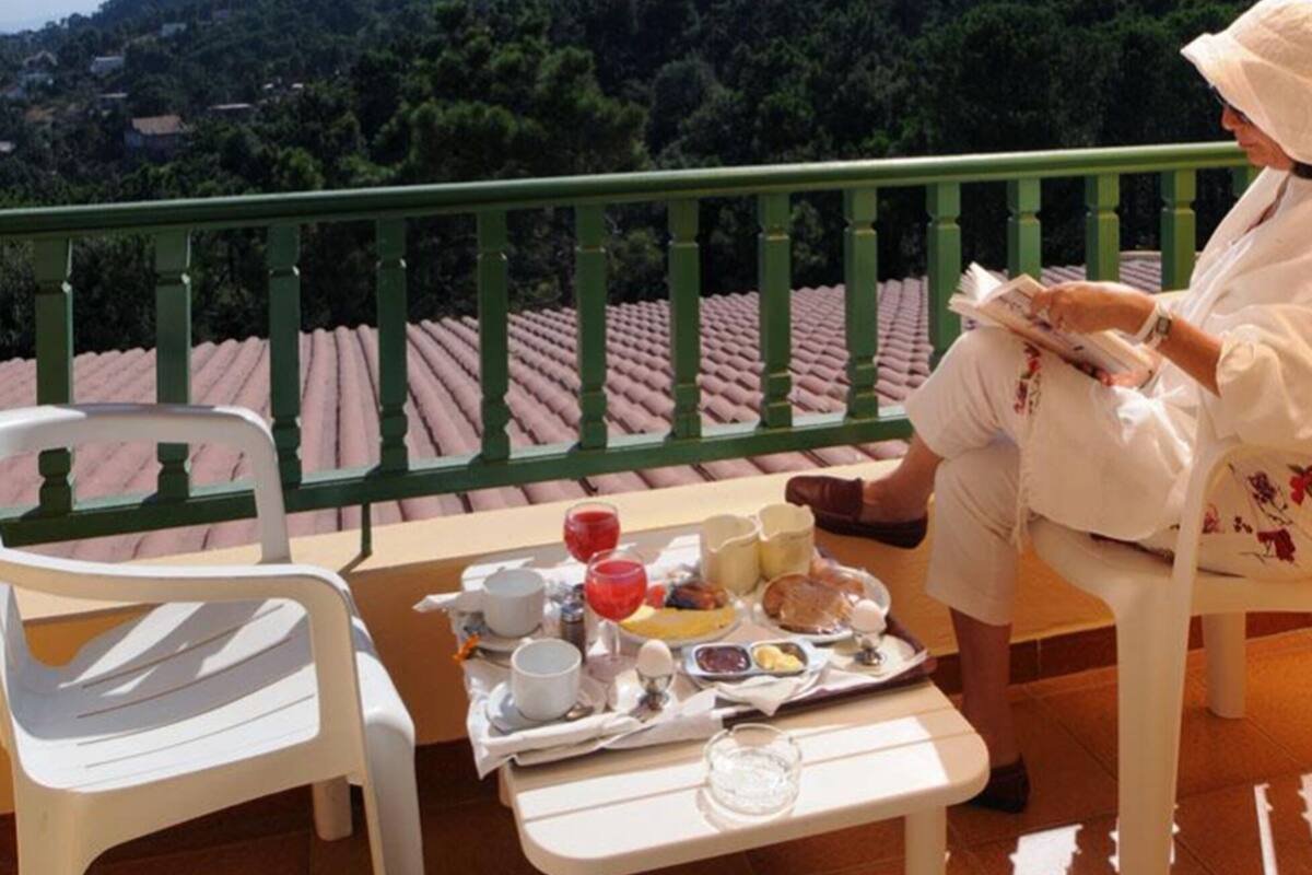 A balcony with a table set for breakfast, a chair, and a person reading a book.