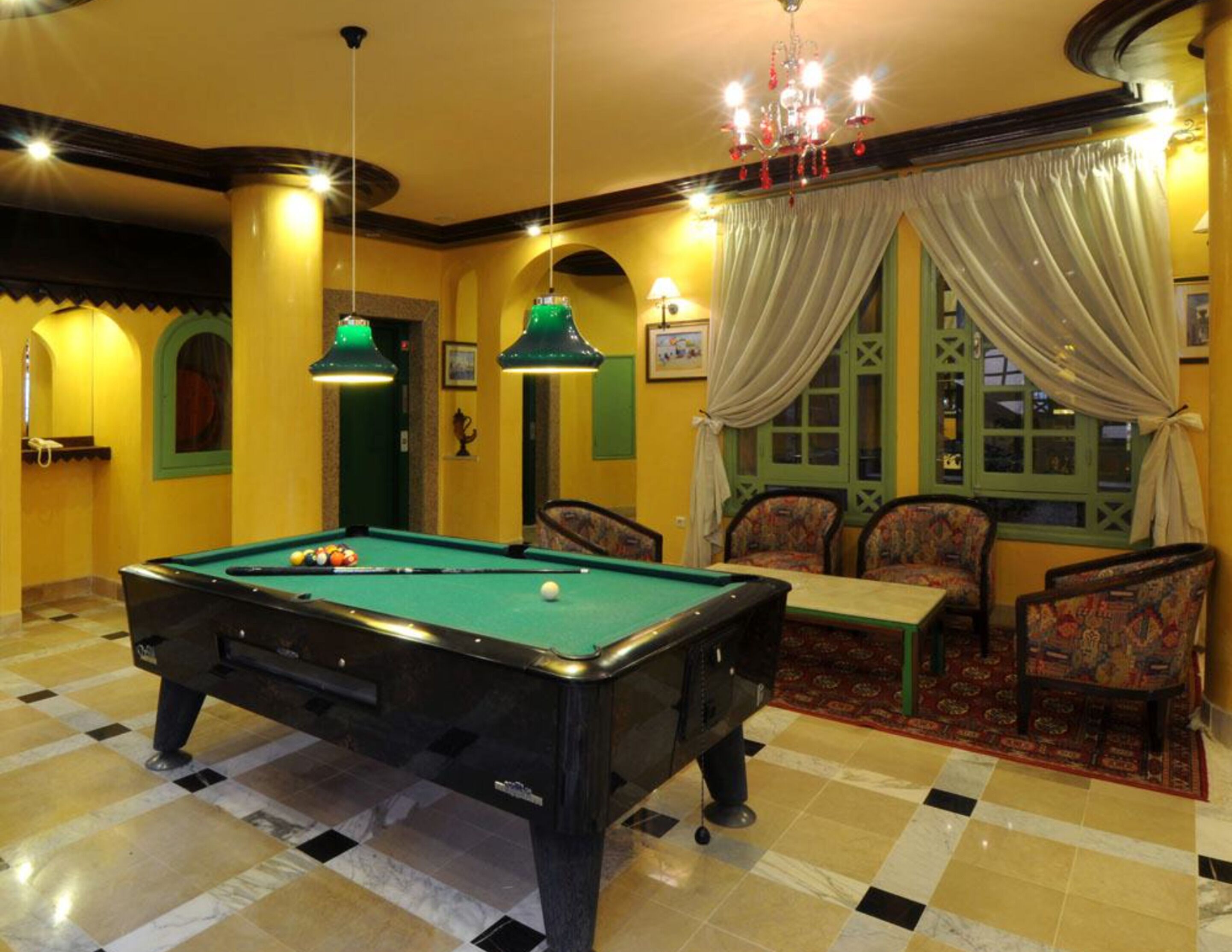 A pool table in a room with yellow walls, patterned chairs, and a chandelier.
