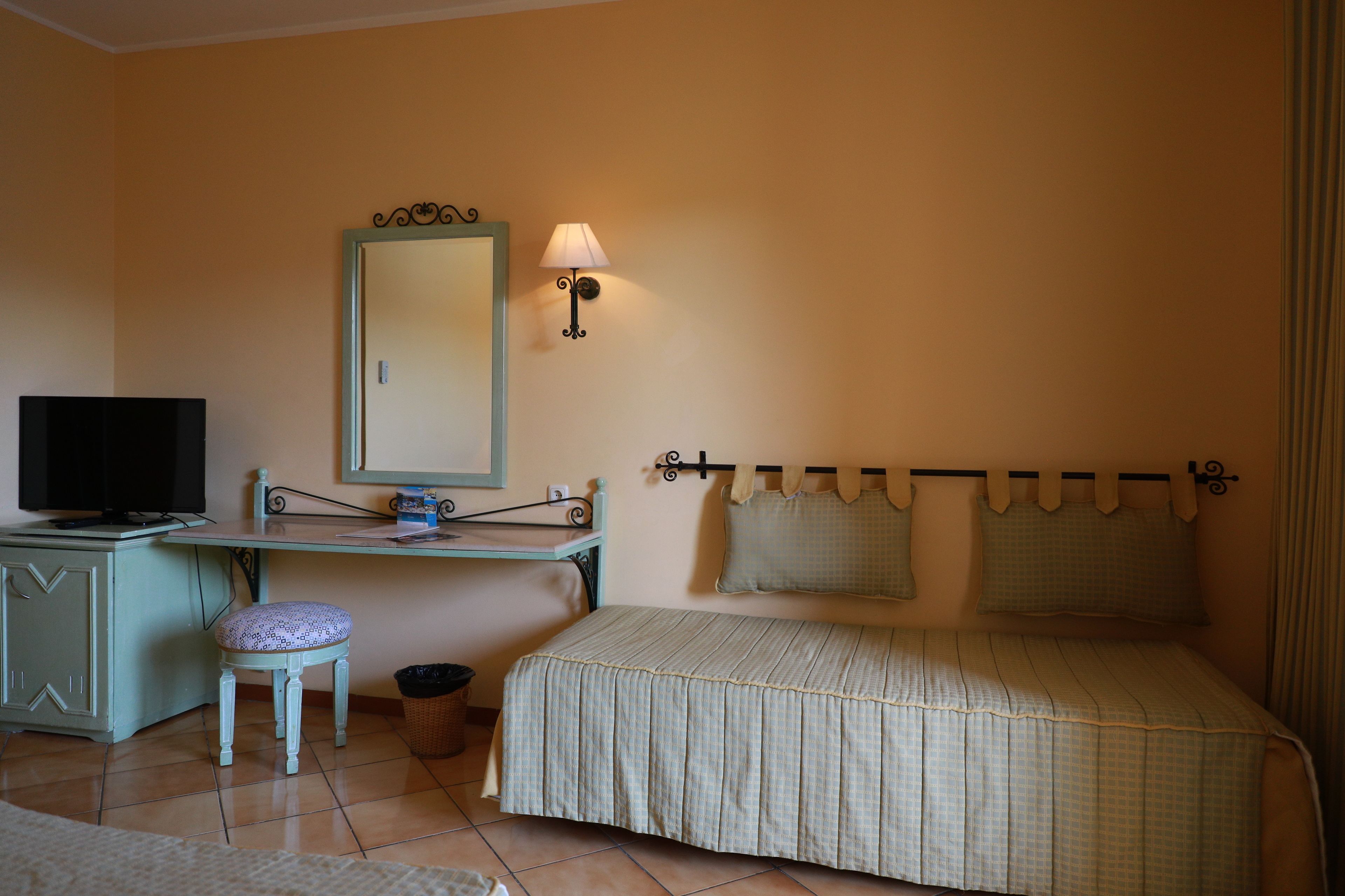 A bedroom with a bed, a desk, a chair, a television, and a wall-mounted lamp.